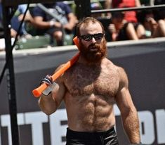 a shirtless man holding an orange baseball bat in his right hand and wearing sunglasses