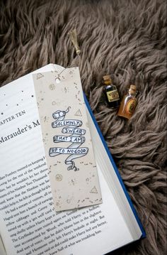 an open book sitting on top of a fur covered floor next to two small bottles