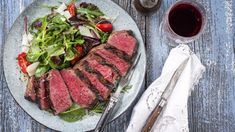 a plate with steak and salad on it next to a glass of wine, fork and knife