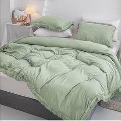 a bed with green comforter and pillows on it in a room next to a night stand