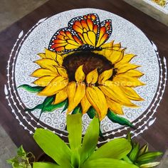 a sunflower painted on a white plate with a butterfly sitting on the center piece