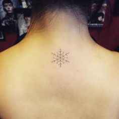 the back of a woman's neck with a small snowflake tattoo on it