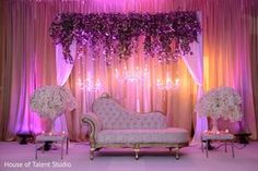 a couch and some chairs in front of a stage with flowers on the back wall