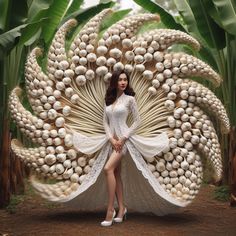 a woman standing in front of a giant peacock made out of eggs and shells with her legs crossed