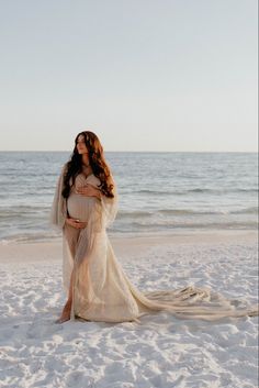 a woman standing on top of a sandy beach next to the ocean wearing a white dress