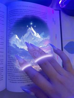 a woman's hand holding an open book in front of a mountain scene with stars