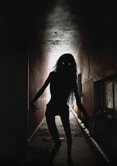 a woman walking down a dark hallway with her arms outstretched