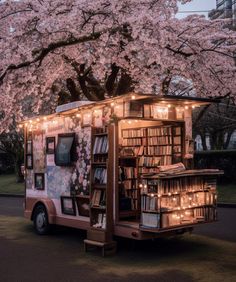 a pink food truck parked in front of a tree with lots of books on it