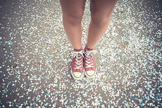 a person standing on the ground with their legs crossed and wearing red converses, surrounded by confetti