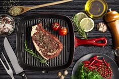 a steak on a grill with vegetables and seasoning next to it, surrounded by other cooking utensils