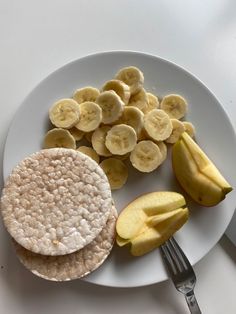 a white plate topped with sliced bananas and crackers next to a knife and fork