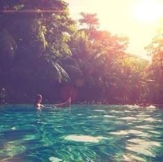 a person in a pool with trees and sun shining on the water behind them,