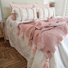 a white bed topped with pink and white pillows next to a wooden floor covered in blankets