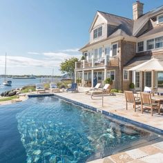 an outdoor swimming pool with chairs and umbrellas next to a house near the water