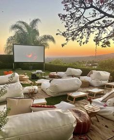 an outdoor movie is set up in the grass with white pillows and chairs around it