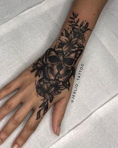 a woman's hand with a skull and flowers tattoo on it