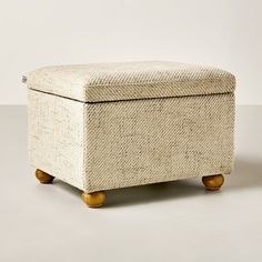 an upholstered footstool with wooden legs on a plain surface in front of a white wall