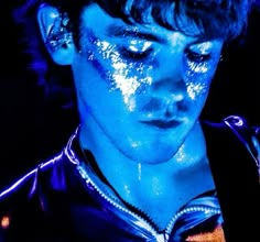 a young man with his eyes closed while he is covered in blue light and glitter