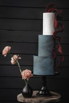 three tiered cake sitting on top of a wooden table with flowers in front of it