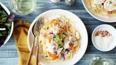 two plates of pasta with meat and vegetables on the side, next to a glass of water