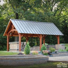 a gazebo in the middle of a park surrounded by trees and shrubs with an outdoor kitchen