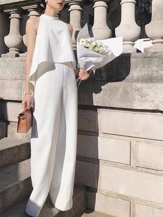 a woman is standing on the steps with flowers in her hand and wearing a white jumpsuit