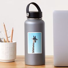 a giraffe sticker on a water bottle next to a cup and laptop