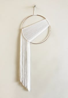 a white wall hanging on the side of a wall with a circular frame and tassels