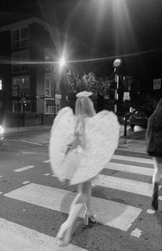 a woman walking across a cross walk holding an angel wings in her hand and wearing high heels