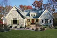 a stone house with green shutters on the front and side windows, surrounded by fall foliage