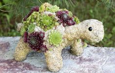 a small stuffed turtle covered in flowers on top of a rock