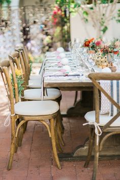 a long table with white chairs and flowers on it