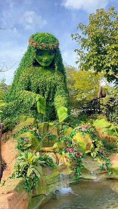 a garden with plants and water in the shape of a woman sitting on top of a rock