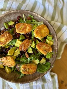 a salad with avocado and other vegetables in a wooden bowl on a striped cloth