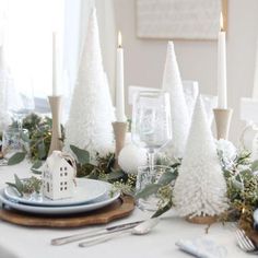 a dining room table decorated for christmas with white trees and greenery on the place setting