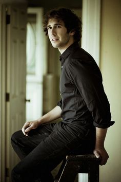 a young man sitting on top of a stool in front of a white door and looking off to the side