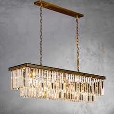 a rectangular chandelier hanging from a chain on a gray wall with gold trim