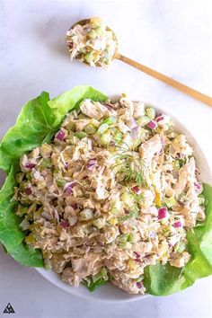 a white plate topped with lettuce and chicken salad next to a wooden spoon