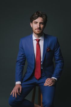 a man in a blue suit and red tie sitting on a chair with his legs crossed