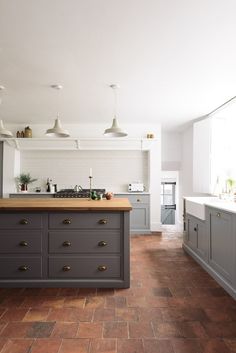 a kitchen with grey cabinets and wooden counter tops, an island in the middle is surrounded by hanging lights