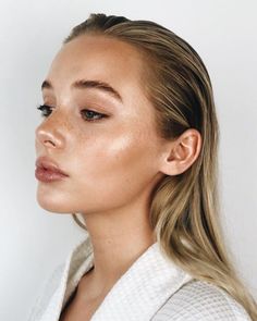 a woman with long blonde hair wearing a white shirt and looking off to the side