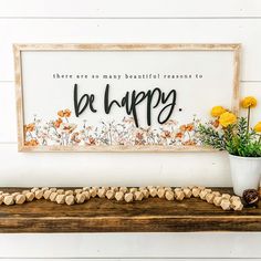 a wooden sign that says be happy next to some flowers and rocks on a shelf