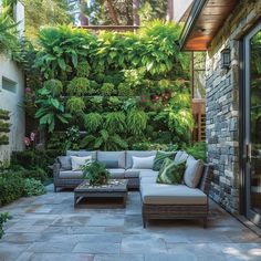 an outdoor living area with couches, tables and greenery on the wall behind it