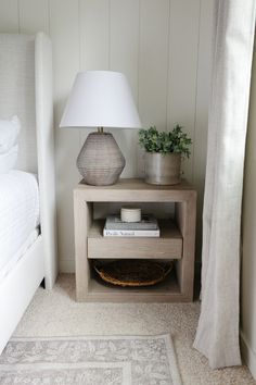 a nightstand with a lamp on it next to a bed