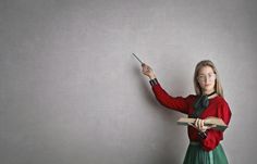 a woman in a red shirt and green skirt is writing on a gray wall with a pair of scissors