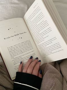 a woman is reading a book while laying on a bed with her hand resting on an open book