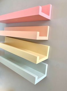 three shelves on the wall are painted different shades of pink, orange and yellow with white trim