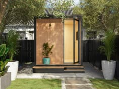 a small wooden structure in the middle of a yard with potted plants and trees