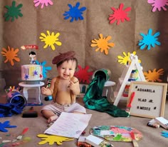 a baby is sitting on the floor in front of some decorations and art supplies that are all around him