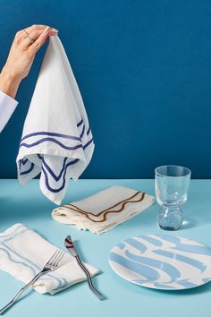 a person holding a napkin over a table with plates and utensils on it